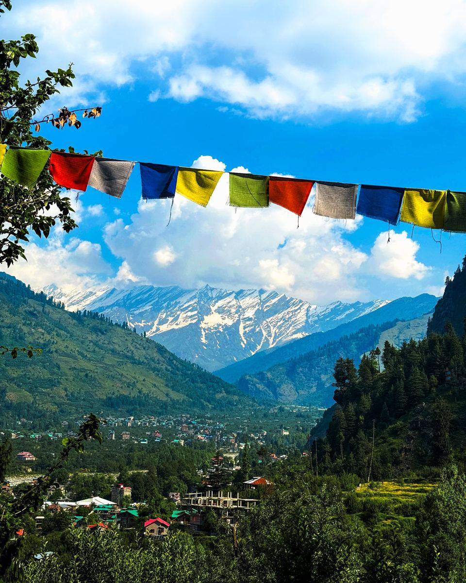Prayer flags above a green valley with snow peaks near Manali
