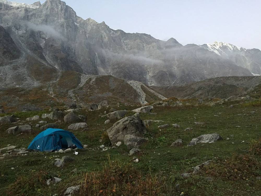 Tent pitched on a rocky meadow below mist-covered cliffs on the Beaskund trail