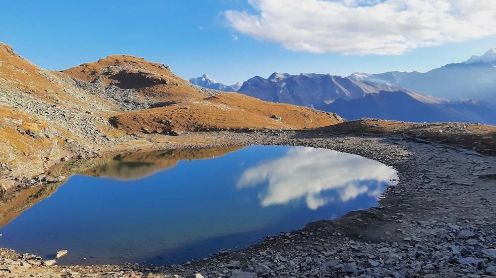 Bhrigu Lake reflecting clouds and blue sky, surrounded by brown alpine slopes