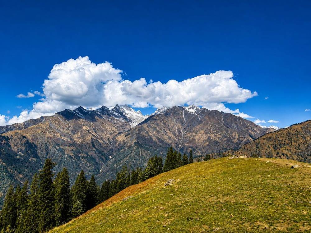 Pine forest and grassy ridges below snow-dusted peaks above the Parvati Valley