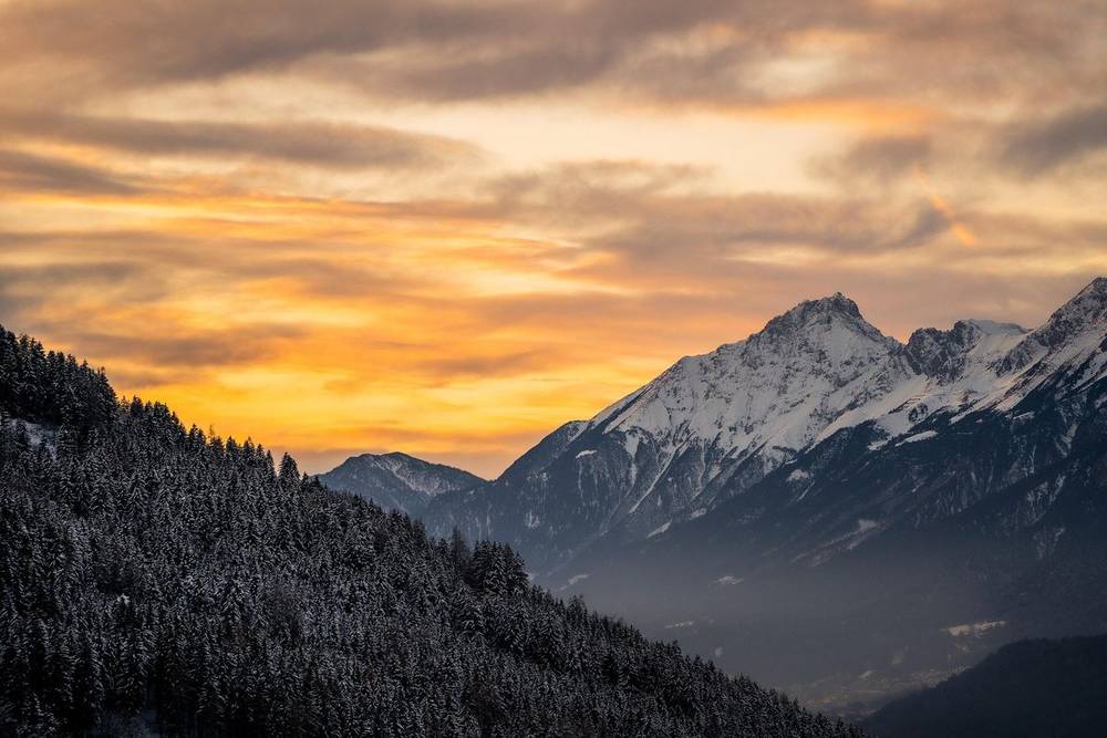 Golden sunset sky over a forested valley and snow peak on the Dev Ropa route