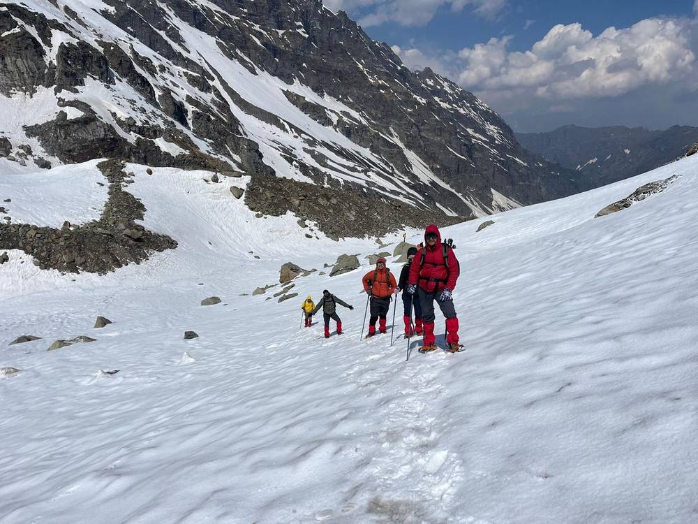 Trekkers crossing a snowfield below steep mountains on the Hampta Pass route