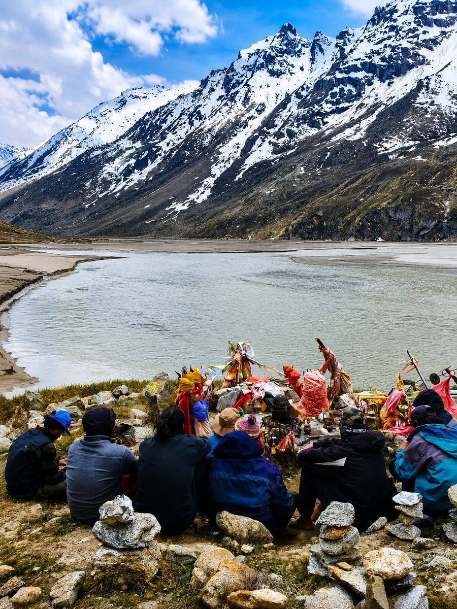 Group of trekkers resting beside the partly frozen Mantalai Lake below snow peaks