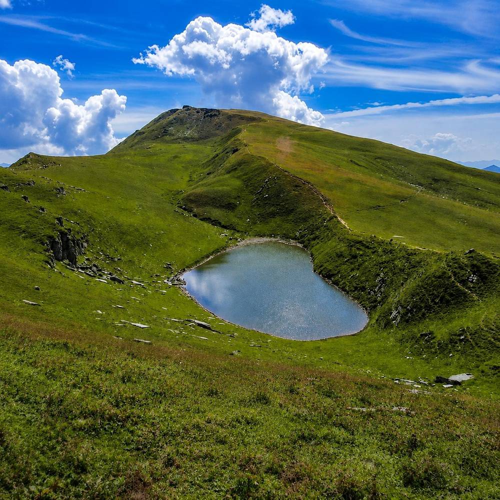 Heart-shaped Rani Sui Lake in a green alpine meadow below a grassy summit
